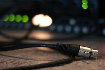 XLR-Kabel – Professionelle Audiotechnik XLR-Audiokabel mit Metallstecker, im Vordergrund liegend, mit unscharfem Mischpult und leuchtenden LED-Anzeigen im Hintergrund.